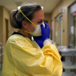 Registered nurse Chrissie Burkhiser puts on personal protective equipment as she prepares to treat a COVID-19 patient in the in the emergency room