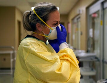 Registered nurse Chrissie Burkhiser puts on personal protective equipment as she prepares to treat a COVID-19 patient in the in the emergency room