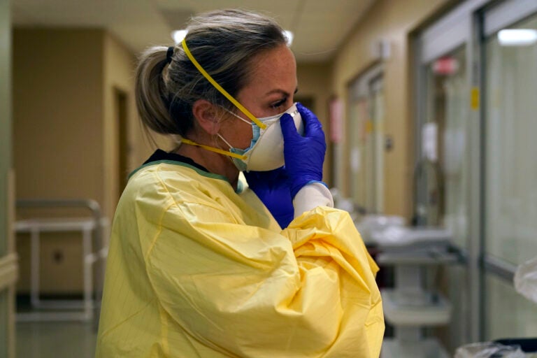 Registered nurse Chrissie Burkhiser puts on personal protective equipment as she prepares to treat a COVID-19 patient in the in the emergency room