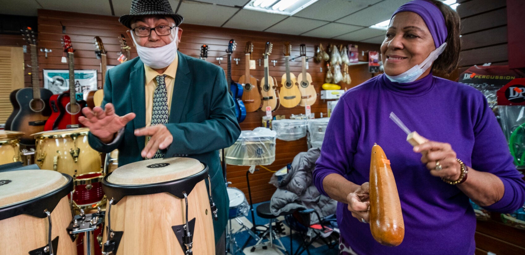 José “Cheo” Rivera and Rosita Benitez playing the bongos and güiro together inside the shop. | José “Cheo” Rivera y Rosita Benitez tocando juntos los bongos y el güiro dentro de la tienda. (Photo by Bernardo Morillo for WHYY)