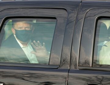 President Trump waves from the back of a car in a motorcade outside of Walter Reed Medical Center in Bethesda, Maryland