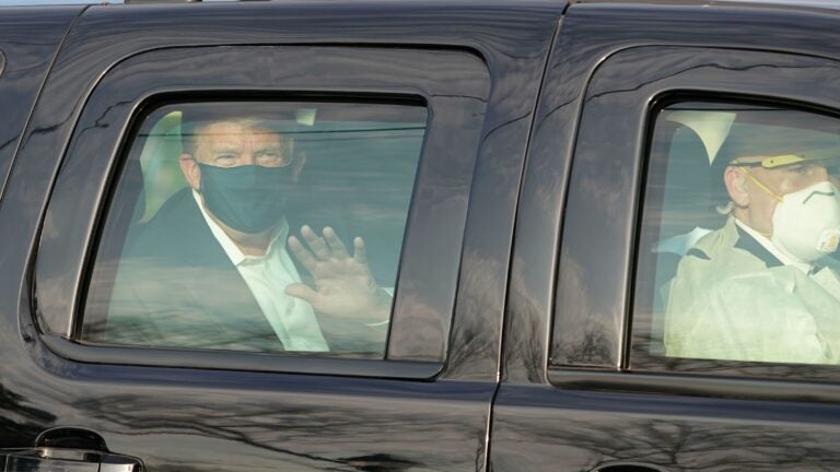 President Trump waves from the back of a car in a motorcade outside of Walter Reed Medical Center in Bethesda, Maryland