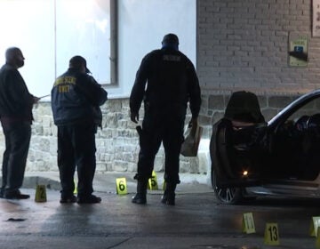 Detectives look at the ground as evidence markers lay on the ground surrounding a vehicle following a fatal carjacking in North Philadelphia.