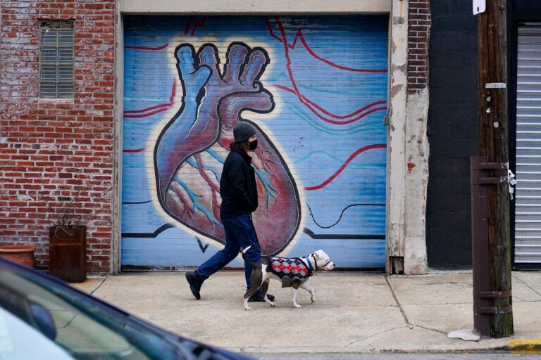 A man wearing a face mask to protect against the spread of the coronavirus walks with a dog