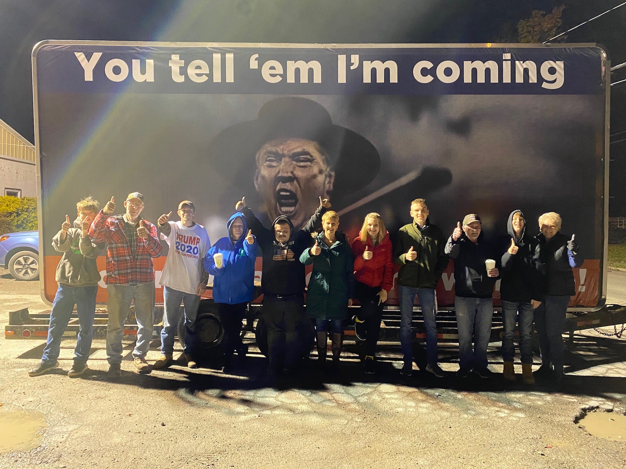 Trump supporters stand under an image of President Trump with text that says "You tell 'em I'm coming" in Lycoming County