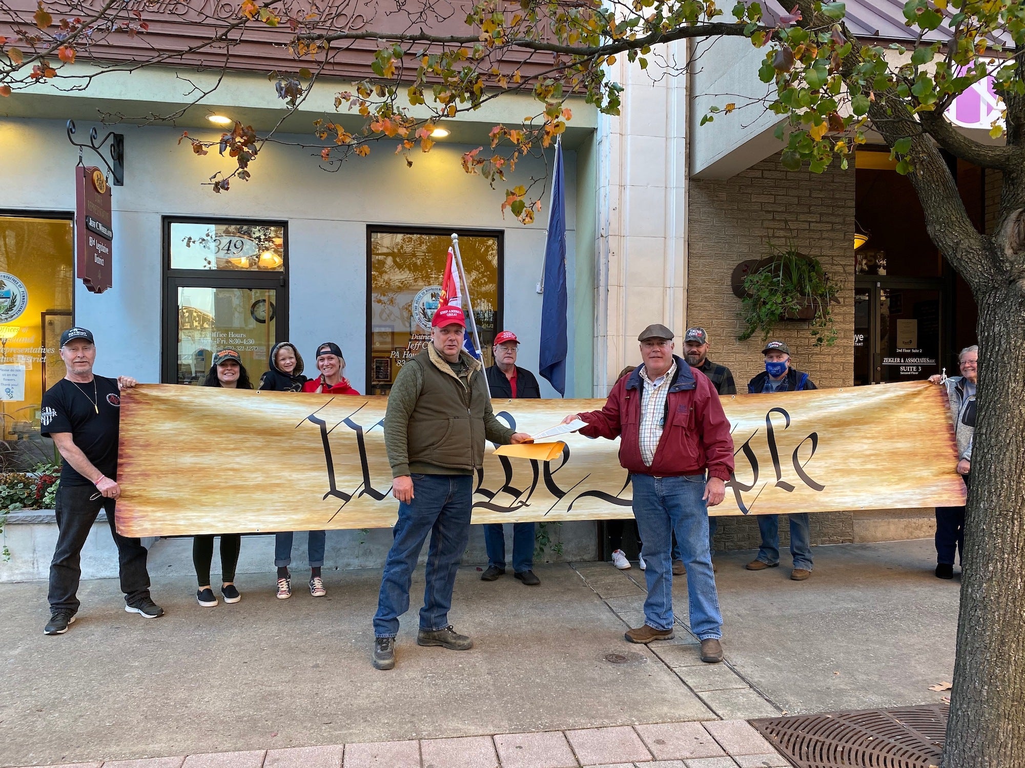 Protesters carrying a banner reading "We the people" rally outside Rep. Jeff Wheeland's office