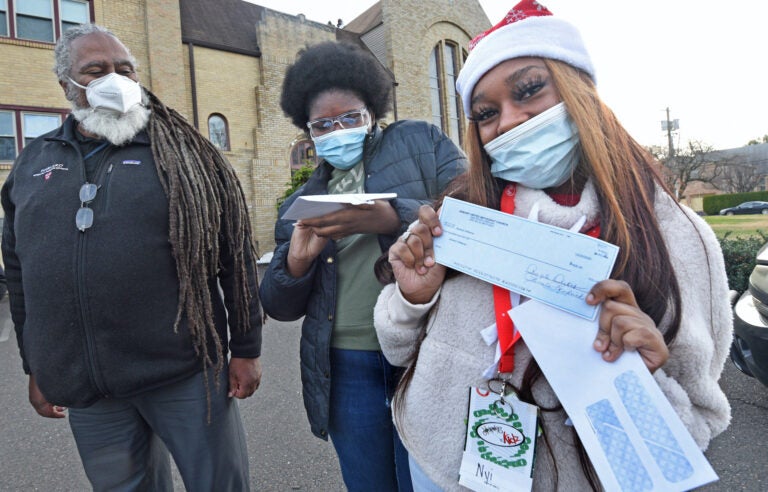 On Dec. 23, Janiayh Williams shows off a check for $400 she's just received from Pastor Tim Merrill in front of the Asbury Community Church in Woodlynne, NJ. Merrill is at left; in the middle is Eternity Easterling, who was also given a check for the census work the teens did in Camden in the summer and for which they were not fully paid. (April Saul for WHYY)
