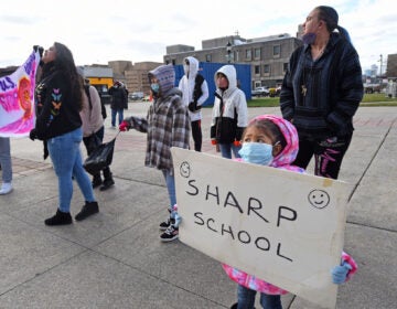 At a Jan. 6 protest at Camden's City Hall,  Ivonne Escobedo Rojas, 5, holds up a sign with the name of Sharp School. Sharp is among several public schools in the city that may be closed by the end of this month. (April Saul for WHYY)