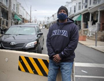 Derrick Smith, wearing a face mask, stands on Simpson Street in front of a traffic barrier
