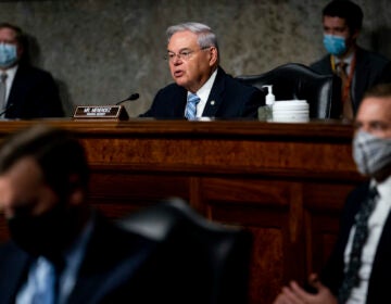 Sen. Menendez sits at a mahogany bench, speaking into a microphone.