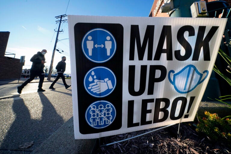 Pedestrians walk past a sign on in Mount Lebanon, Pa.,reminding people to wear a mask, wash their hands and practice social distancing, Wednesday, Nov. 18, 2020. (AP Photo/Gene J. Puskar)