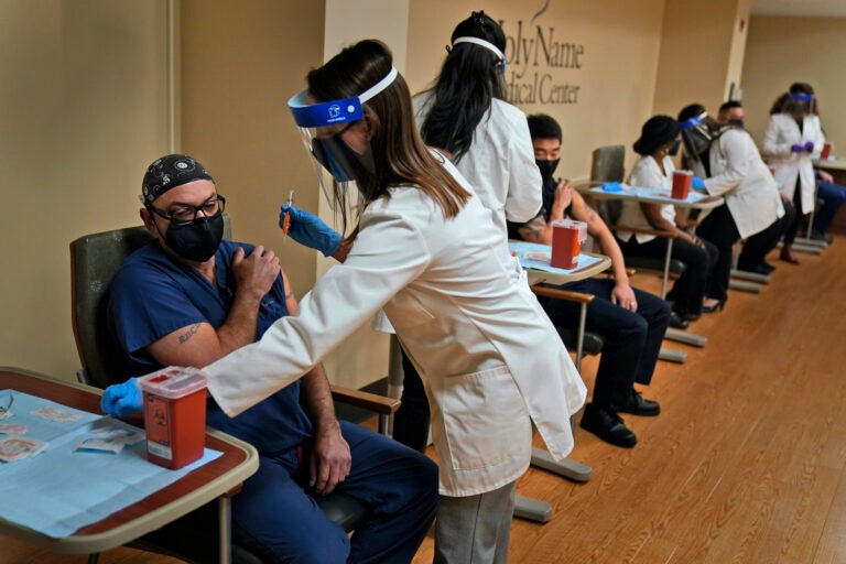 Nurse Reynaldo Pella, left, was one of five staff members to simultaneously receive the first doses of the COVID-19 vaccine at Holy Name Medical Center in Teaneck, N.J., Thursday, Dec. 17, 2020. The hospital received almost 1000 doses of the vaccine in the middle of a snowstorm which blanketed much of the Northeast in snow. (AP Photo/Seth Wenig)