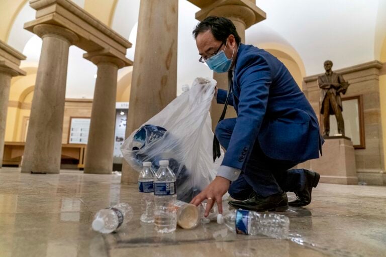 Rep. Andy Kim, D-N.J., cleans up debris and trash strewn across the floor in the early morning hours after protesters stormed the Capitol in Washington, Thursday, Jan. 7, 2021. (AP Photo/Andrew Harnik)