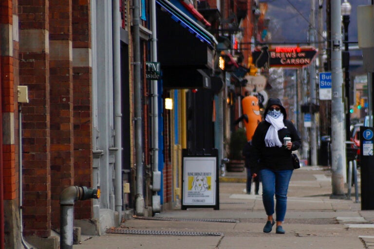 People wearing protective masks walk past businesses and apartments along East Carson Street