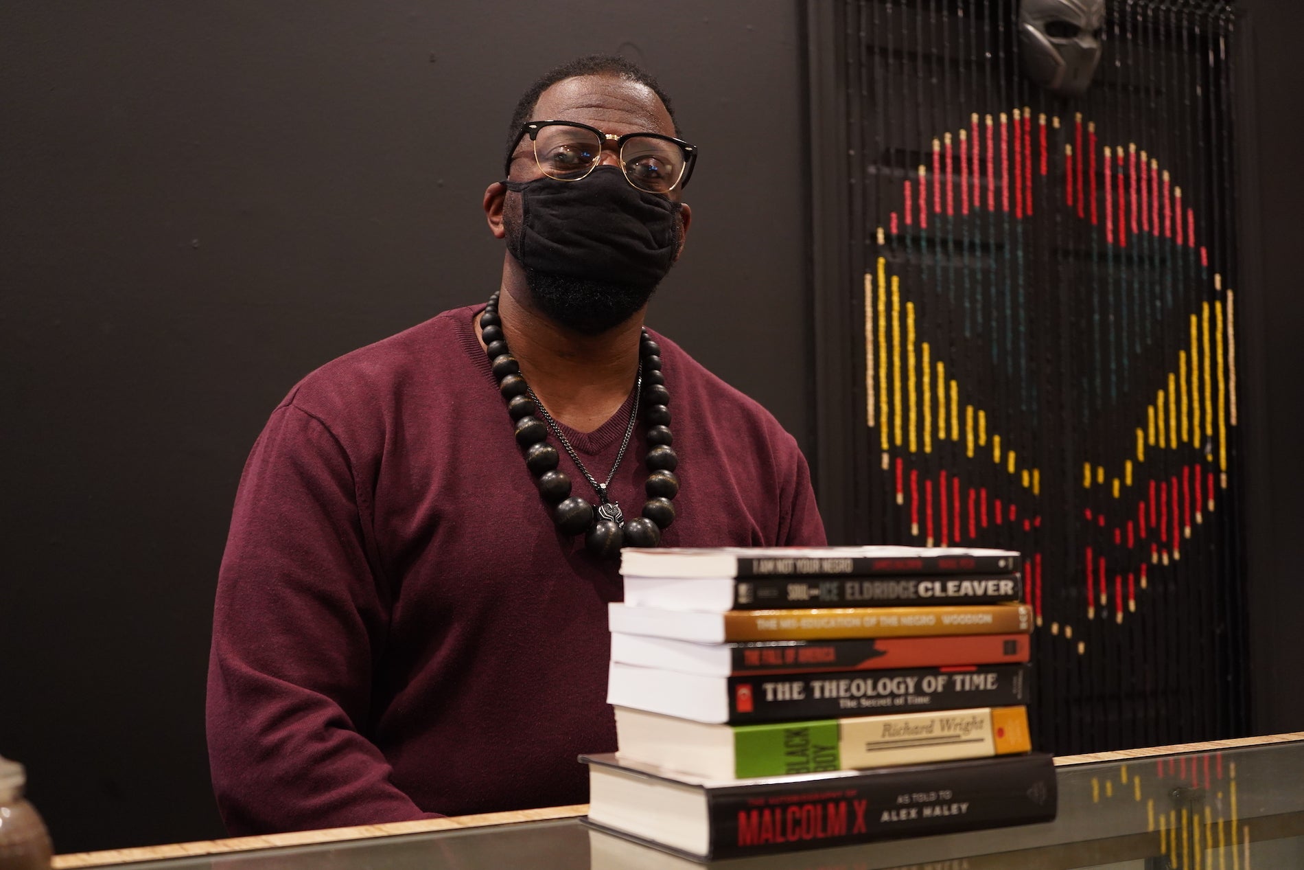 Shaykh Anwar Muhammad wears a face mask, with a stack of books in front of him