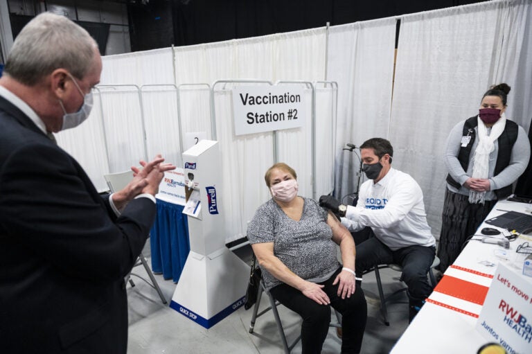 Phil Murphy, New Jersey's governor, left, applauds after a person receives a dose of a Covid-19 vaccination at the New Jersey Convention and Exposition Center in Edison, New Jersey, U.S., on Friday, Jan. 15, 2021. New Jersey will expand Covid-19 vaccinations to people 65 years old and over and those ages 16 to 64 who have 