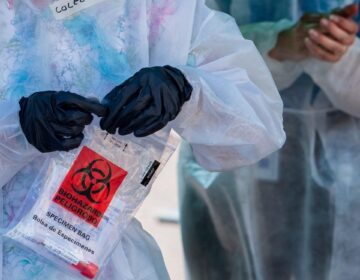 A health care worker holds a sample from a coronavirus test in a sealed plastic bag.