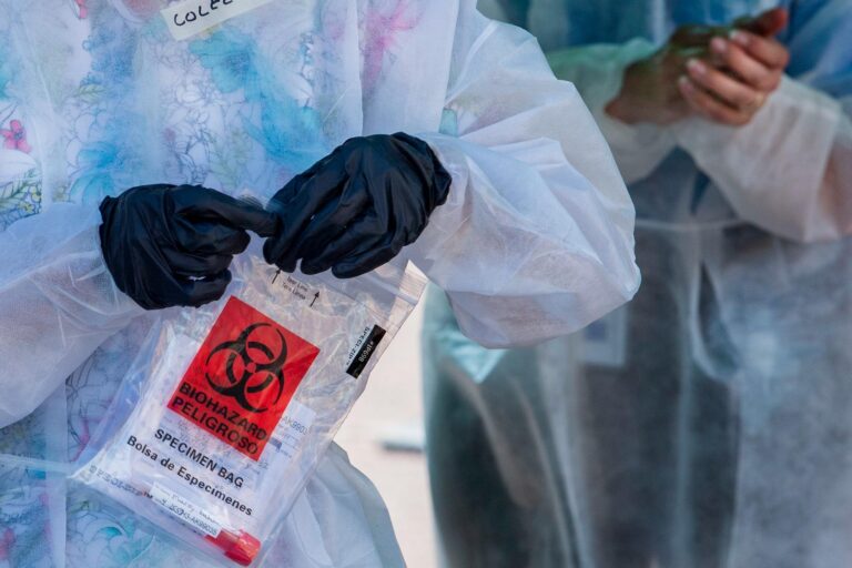 A health care worker holds a sample from a coronavirus test in a sealed plastic bag.