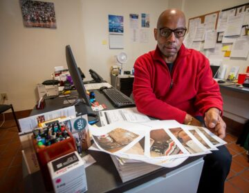 Fred Way sits at his desk with papers strewn across it.