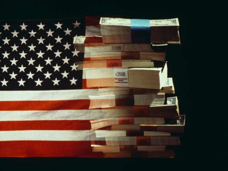 The American flag superimposed over a pile of American dollars banknotes