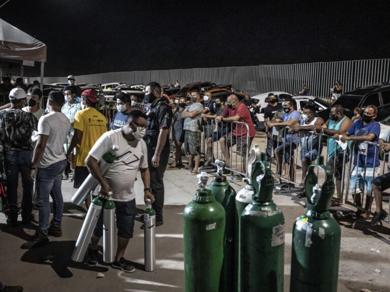 People wearing protective masks wait in line to refill oxygen tanks in Manaus
