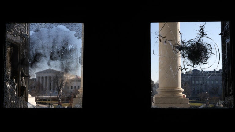 The U.S. Supreme Court is seen through a broken window at an entrance of the U.S. Capitol