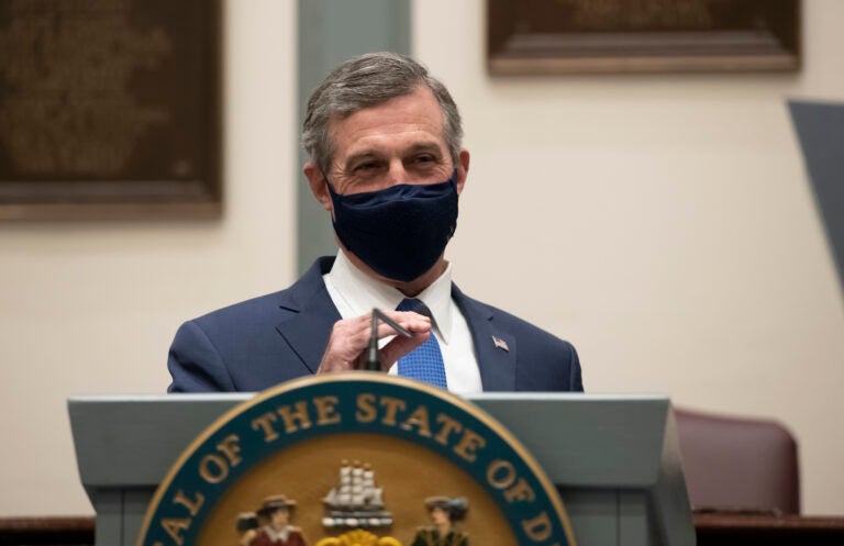 Delaware Gov. John Carney, wearing a face mask, speaks at a podium