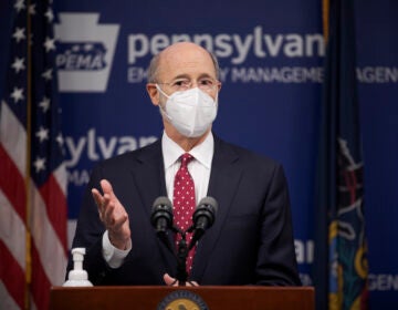 Gov. Tom Wolf, wearing a face mask, speaks to the press from behind a podium