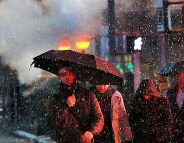 A man holds an umbrella while crossing the street in the snow.