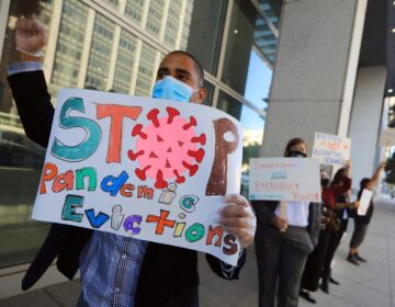 A protester wearing a face mask holds up a sign that says, 