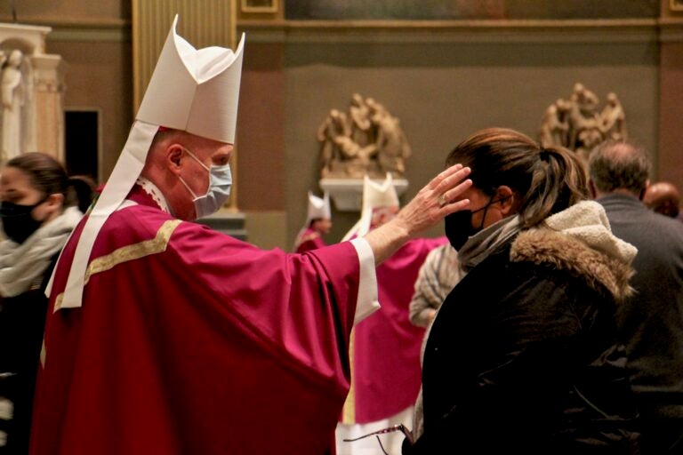 A priest uses his thumb to draw a cross of ashes on the forehead of a parishioner during an Ash Wednesday Mass at the Basilica of Saints Peter and Paul in Philadelphia. (Emma Lee/WHYY)