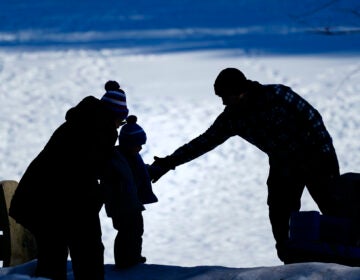 A couple helps a child on a snow covered embankment at Lorimer Park in Huntingdon Valley, Pa., Friday, Feb. 5, 2021. (AP Photo/Matt Rourke)