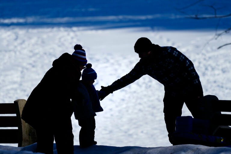 A couple helps a child on a snow covered embankment at Lorimer Park in Huntingdon Valley, Pa., Friday, Feb. 5, 2021. (AP Photo/Matt Rourke)