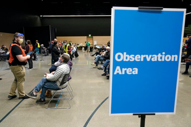 In this  Jan. 24, 2021, file photo, a worker at left checks in with people sitting in an observation area after they were given the first of two doses of the Pfizer vaccine for COVID-19 in Seattle. (AP Photo/Ted S. Warren)