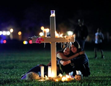 In this Feb. 15, 2018 file photo, people comfort each other as they sit and mourn at one of seventeen crosses, after a candlelight vigil for the victims of the shooting at Marjory Stoneman Douglas High School, in Parkland, Fla.  (AP Photo/Gerald Herbert, File)