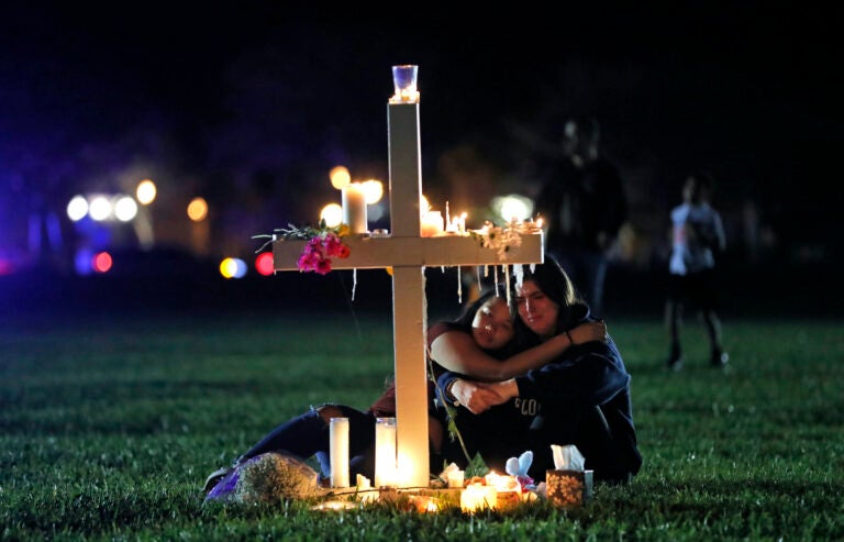 In this Feb. 15, 2018 file photo, people comfort each other as they sit and mourn at one of seventeen crosses, after a candlelight vigil for the victims of the shooting at Marjory Stoneman Douglas High School, in Parkland, Fla.  (AP Photo/Gerald Herbert, File)