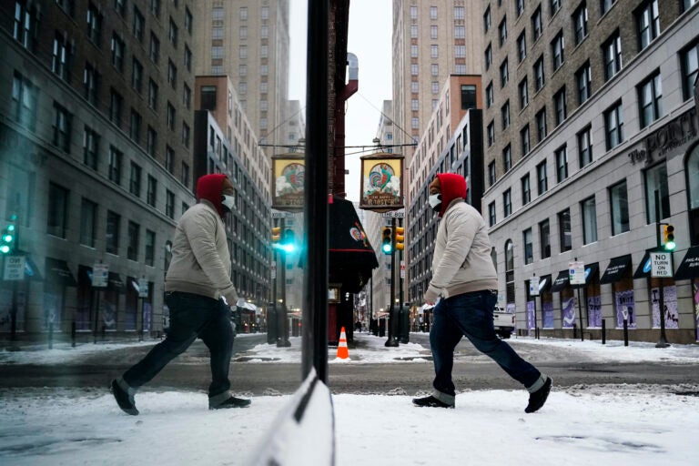 A person, reflected in a window while wearing a face mask as a precaution against the coronavirus, walks during a winter storm in Philadelphia