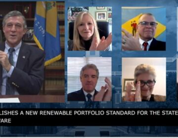 Delaware Gov. John Carney holds a signed copy of legislation mandating an increase in the amount of energy Delaware gets from renewable sources. (State of Delaware screenshot)