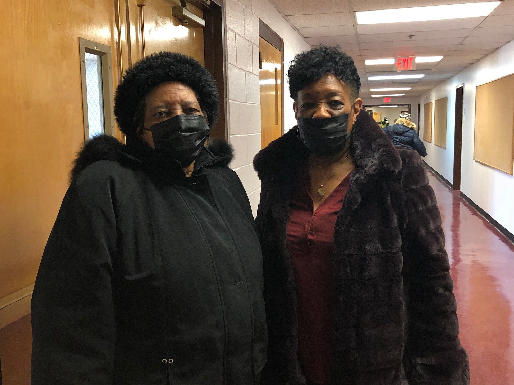 Linda Scott and Mary Lawton, both wearing face masks, stand in a hallfway