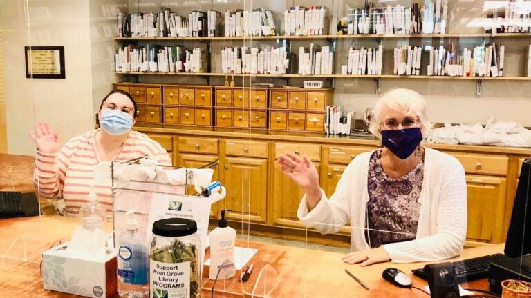 Two women, wearing face masks, sit behind a desk at Avon Grove Library.