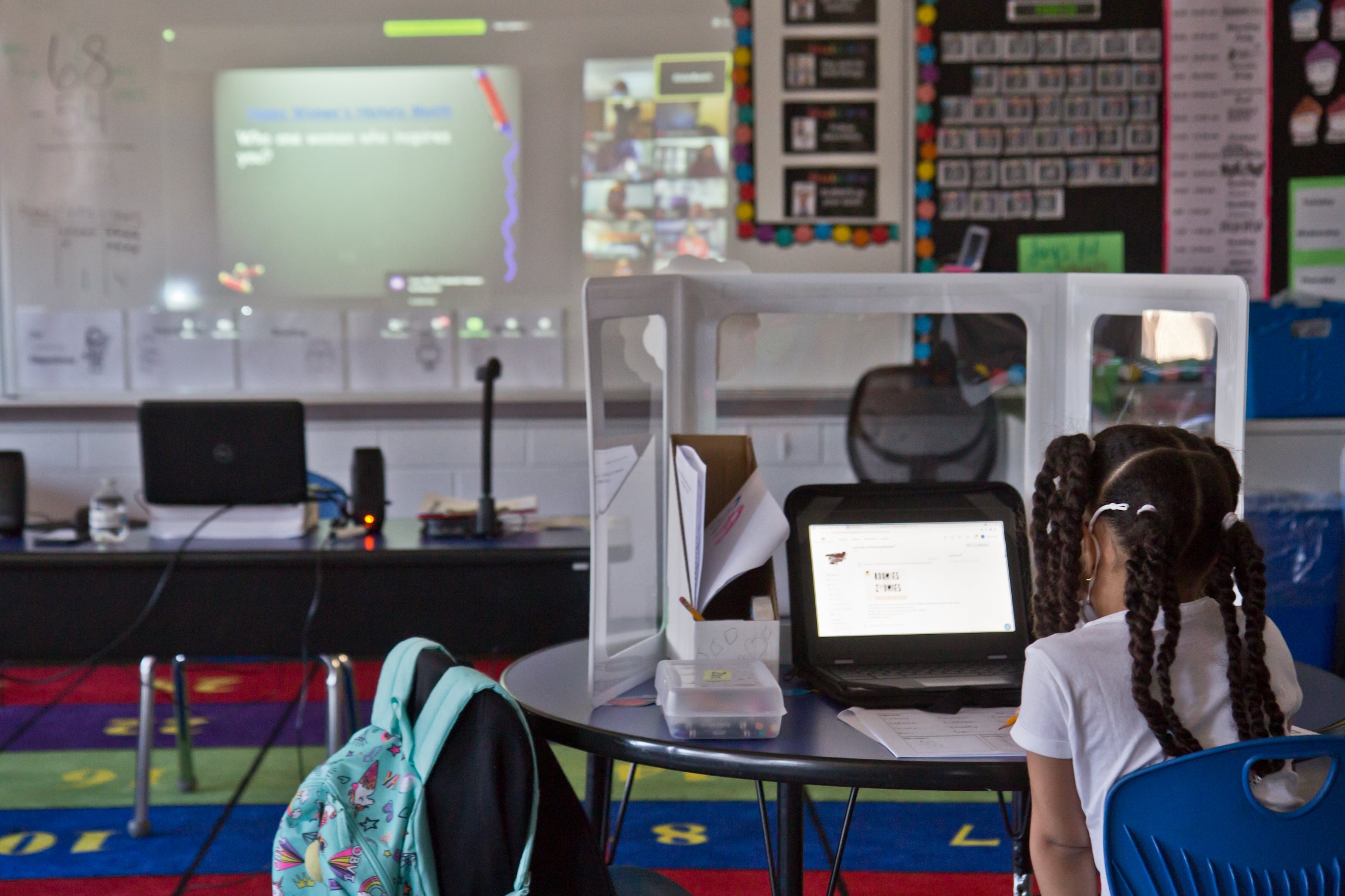 A student, wearing a face mask, sits at an isolated desk at school