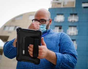 Joseph Ortiz, a contact tracer with New York City's Health + Hospitals battling the coronavirus pandemic, uses his tablet to gather information as he heads to a potential patient's home Thursday, Aug. 6, 2020, in New York. The city has hired more than 3,000 tracers and the city says it's now meeting its goal of reaching about 90% of all newly diagnosed people and completing interviews with 75%. (AP Photo/John Minchillo)