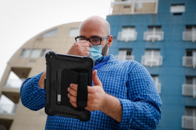 Joseph Ortiz, a contact tracer with New York City's Health + Hospitals battling the coronavirus pandemic, uses his tablet to gather information as he heads to a potential patient's home Thursday, Aug. 6, 2020, in New York. The city has hired more than 3,000 tracers and the city says it's now meeting its goal of reaching about 90% of all newly diagnosed people and completing interviews with 75%. (AP Photo/John Minchillo)