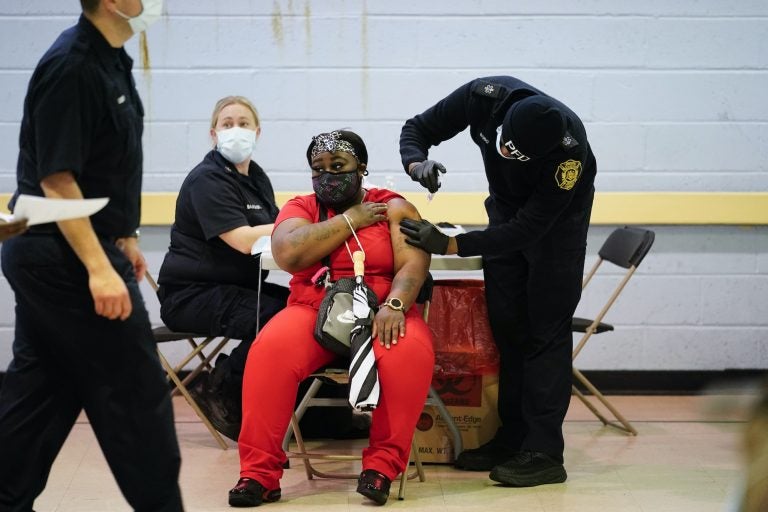 A member of the Philadelphia Fire Department administers the Johnson & Johnson COVID-19 vaccine to a woman at a vaccination site setup