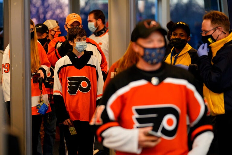 Fans wearing masks walk through security at the Wells Fargo Center