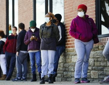 People wearing face masks wait in line to receive COVID-19 vaccines