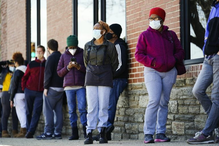People wearing face masks wait in line to receive COVID-19 vaccines