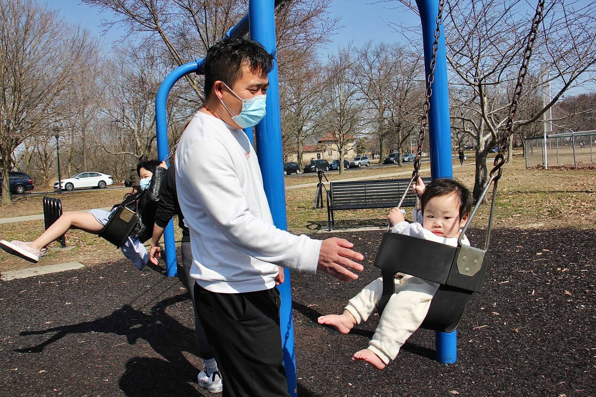 Wu Tan plays with his daughters on a swing set at FDR Park