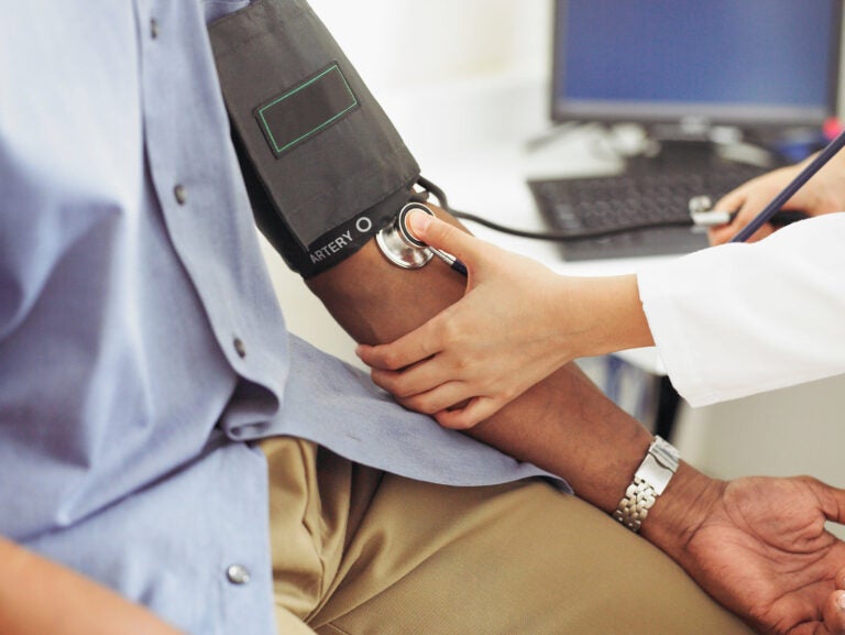 A white health care worker takes the blood pressure of a Black patient