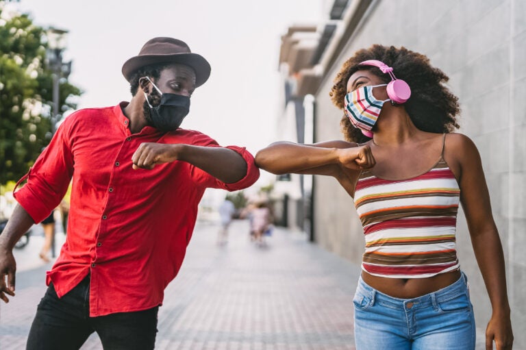 Two friends greeting each other with elbow bumps during the COVID-19 pandemic